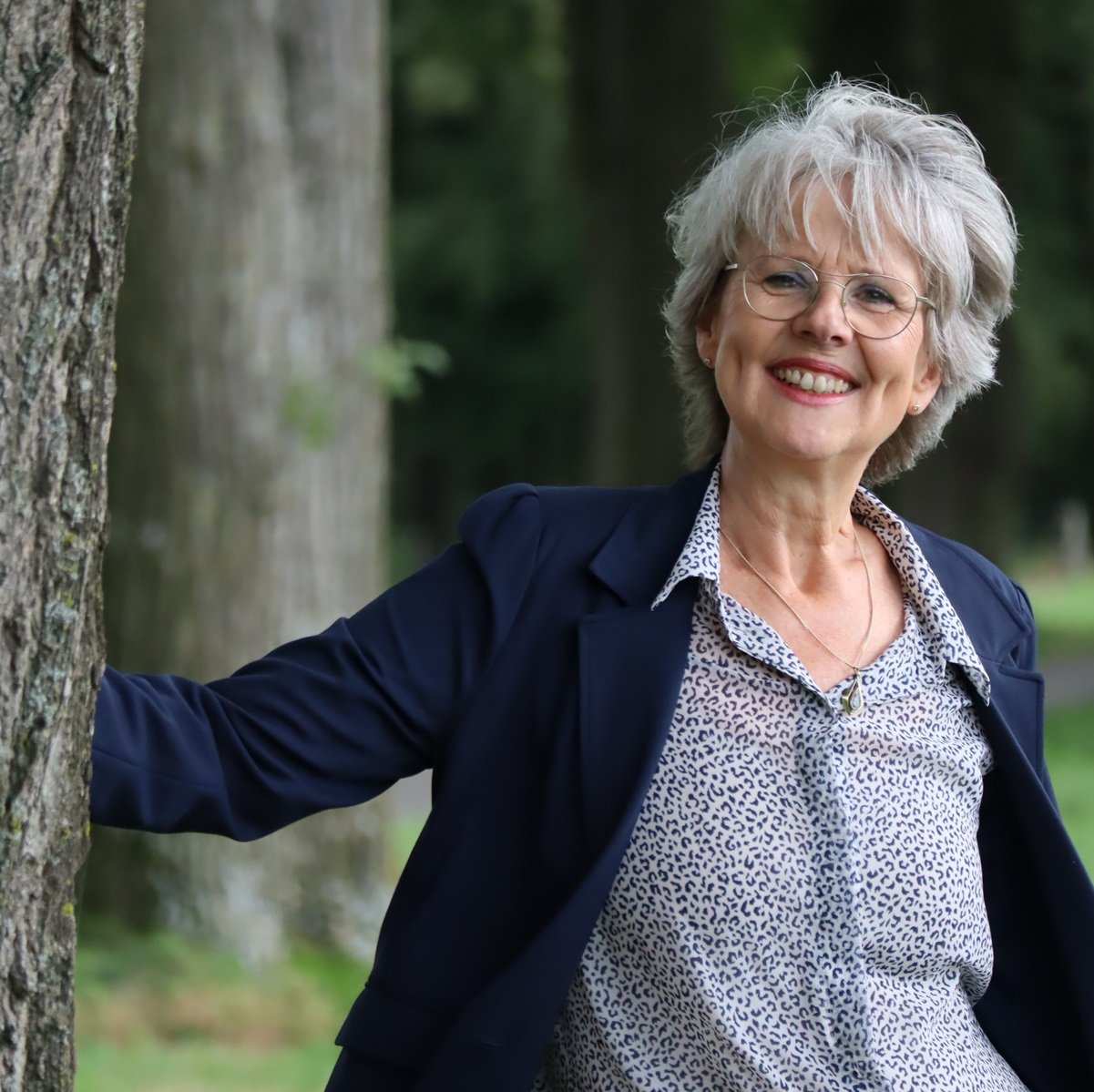 Glimlachende big five for life coach leunend tegen boom in park.